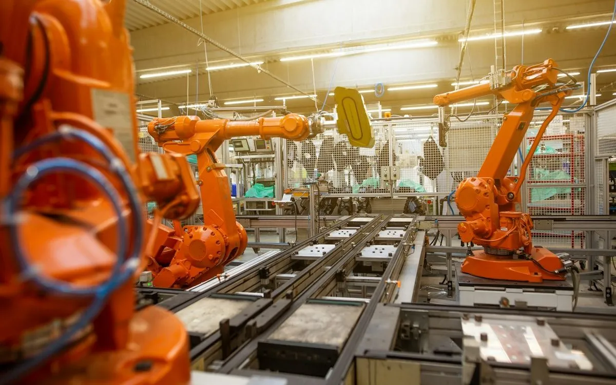 Orange robotic arms working along a factory assembly line.
