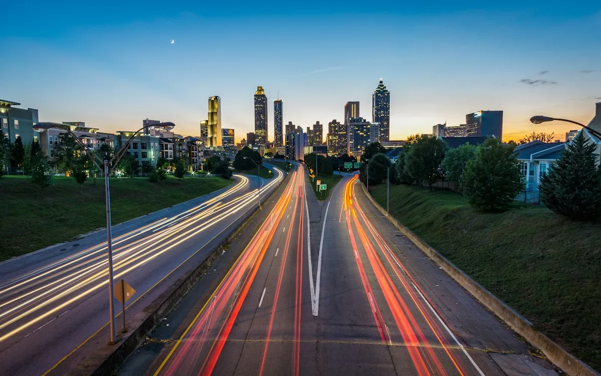 Light trails on a highway leading into a city skyline at dusk.